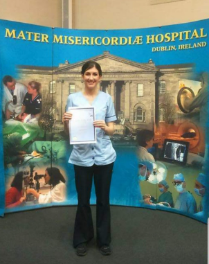 Maire posing with a certificate in front of the Mater Hospital poster