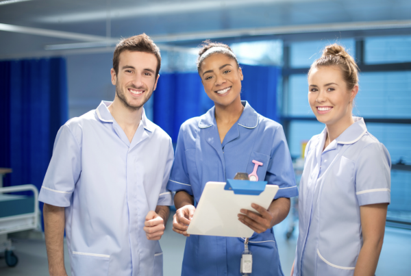 three nurses in scrubs, smiling at the camera