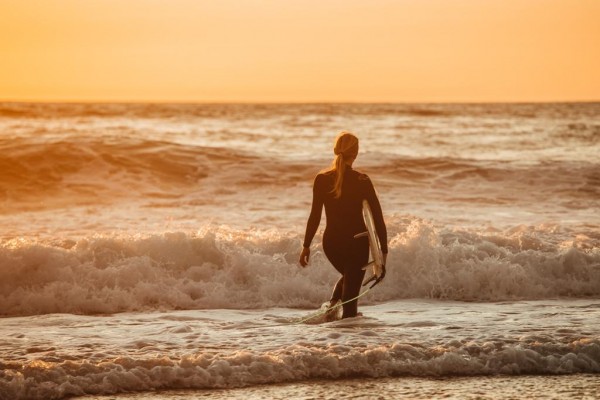 Elaine Breen, carrying her surfboard at sunset